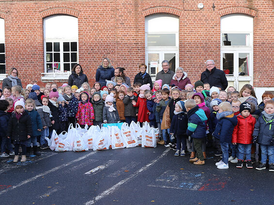 Elèves, professeurs, administrateurs du CCAS et élu(e)s dans la cour de l'école maternelle Suzanne Lanoy posant devant la collecte de denrées alimentaires de l'école.